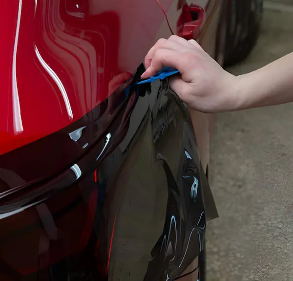 Lustrd Detailing technician applying clear Paint Protection Film (PPF) to a red luxury car in Sydney.