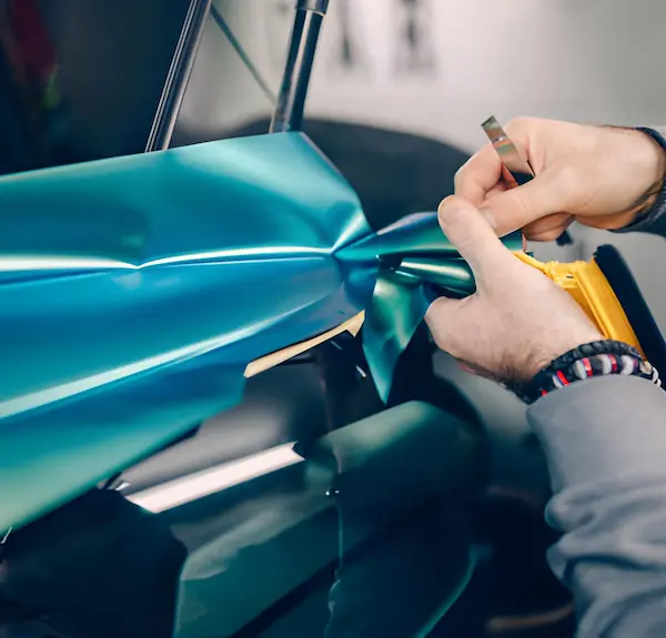 Expert car wrapping at Lustrd Detailing Sydney, showing precision trimming of a teal metallic vinyl wrap on a car wing.